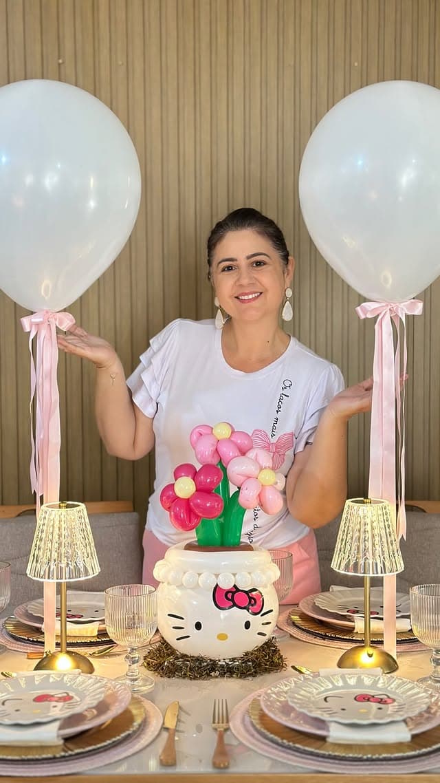Cris sorrindo atrás de mesa decorada com flores de balão